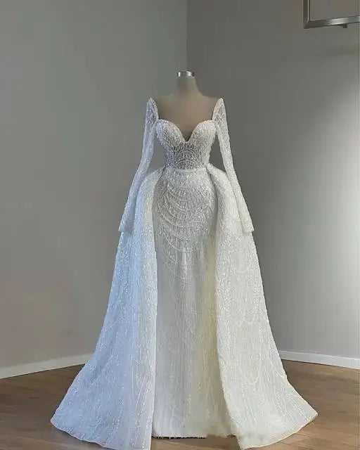 Elegant white bridal gown on a mannequin, featuring long lace sleeves, a structured bodice, and a flowing lace skirt with intricate embroidery, set against a neutral background.