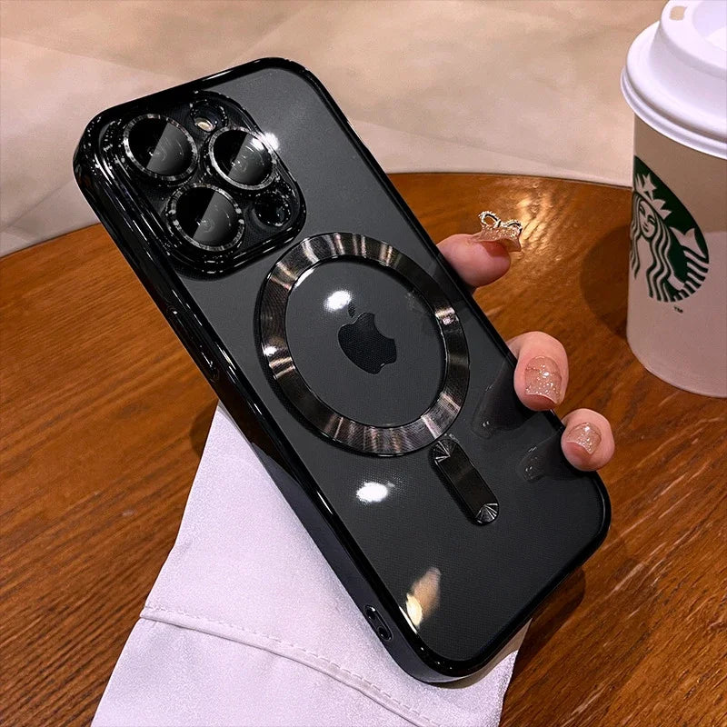 A hand holding a smartphone with a black case featuring a metal ring design on the back. A Starbucks cup sits on a wooden table in the background.