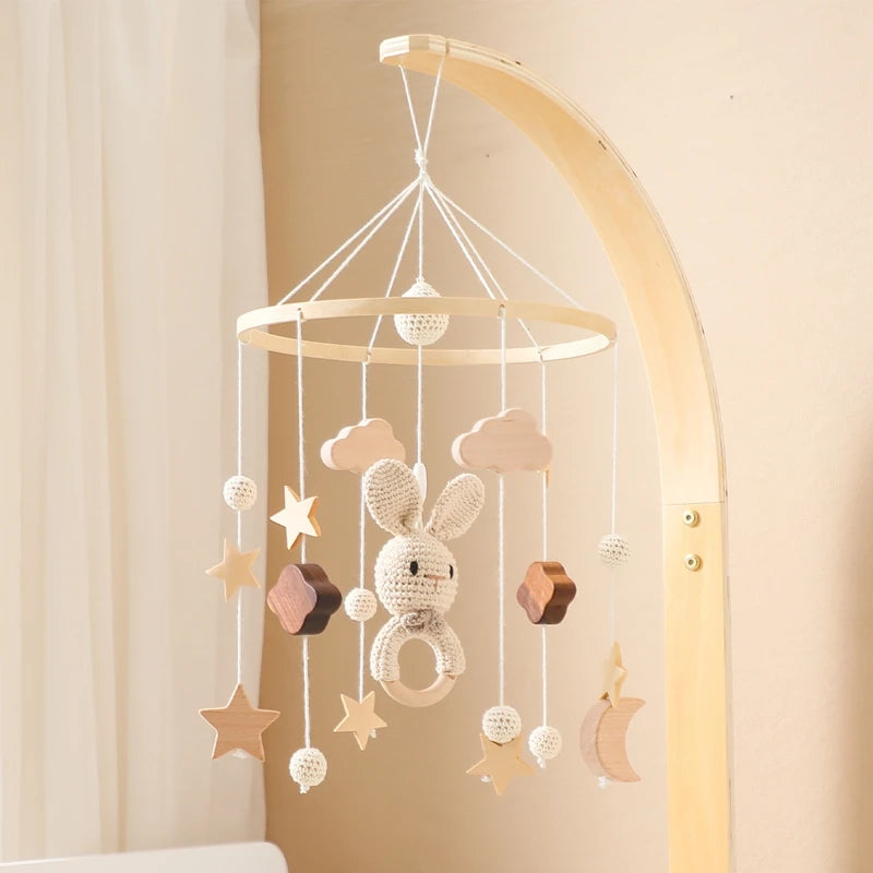Natural wood and crochet baby mobile hanging from a curved stand. Features a crochet bunny, stars, clouds, and moon, in a soft, neutral-colored nursery setting.