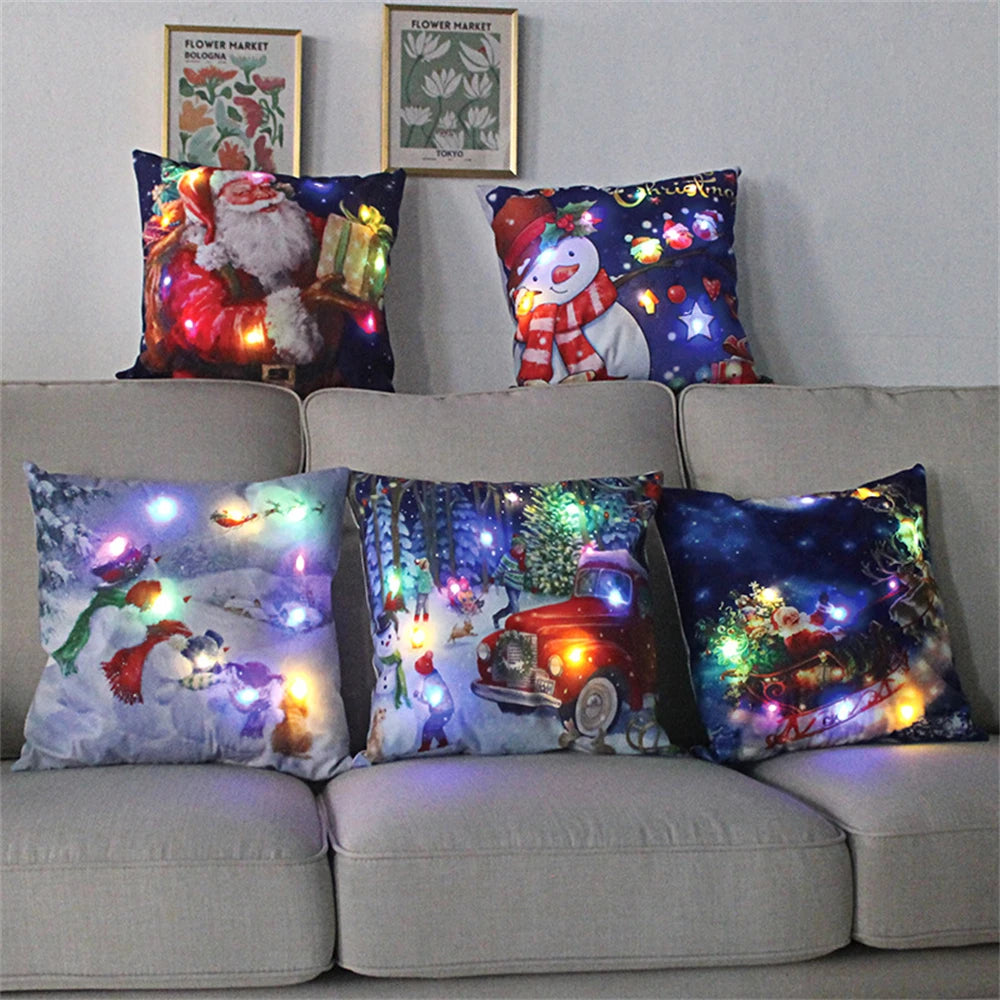 Festive holiday pillows with colorful LED lights depicting Christmas scenes, including Santa, snowmen, and a red truck. Two framed floral prints hang above the couch.