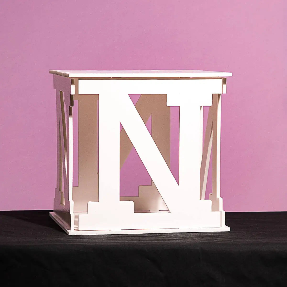 White cube-shaped table with large capital letter "N" design, set against a pink background and resting on a black surface.