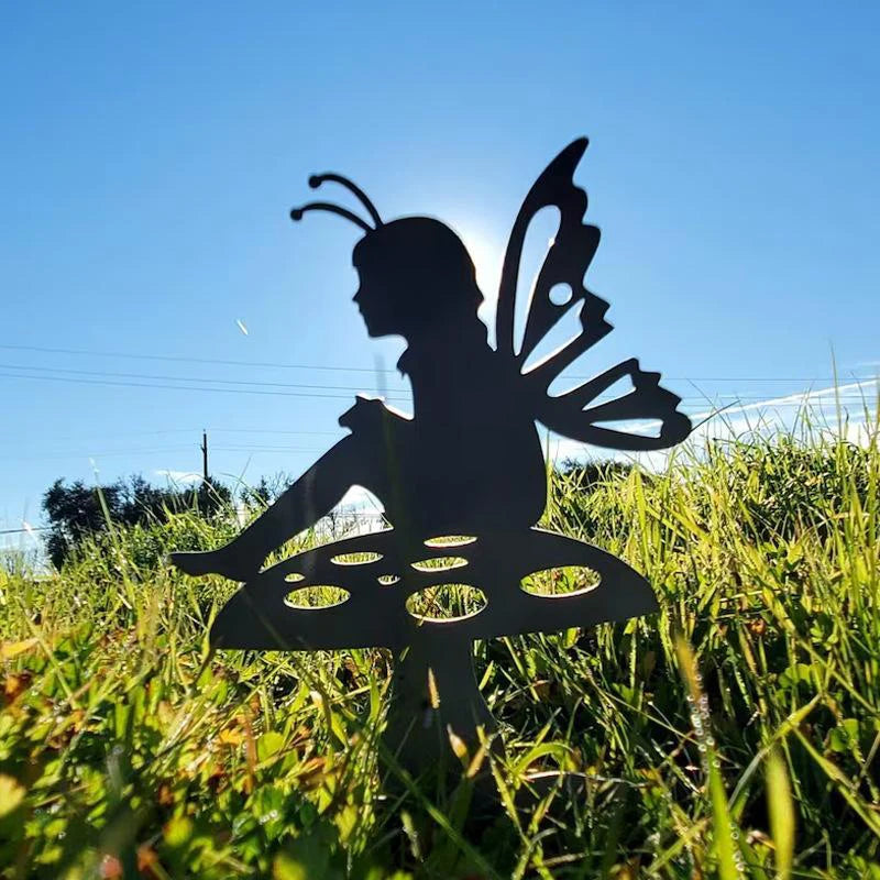 Silhouette of a fairy with wings sitting on a mushroom in a grassy field, backlit by the sun, with a clear blue sky in the background.