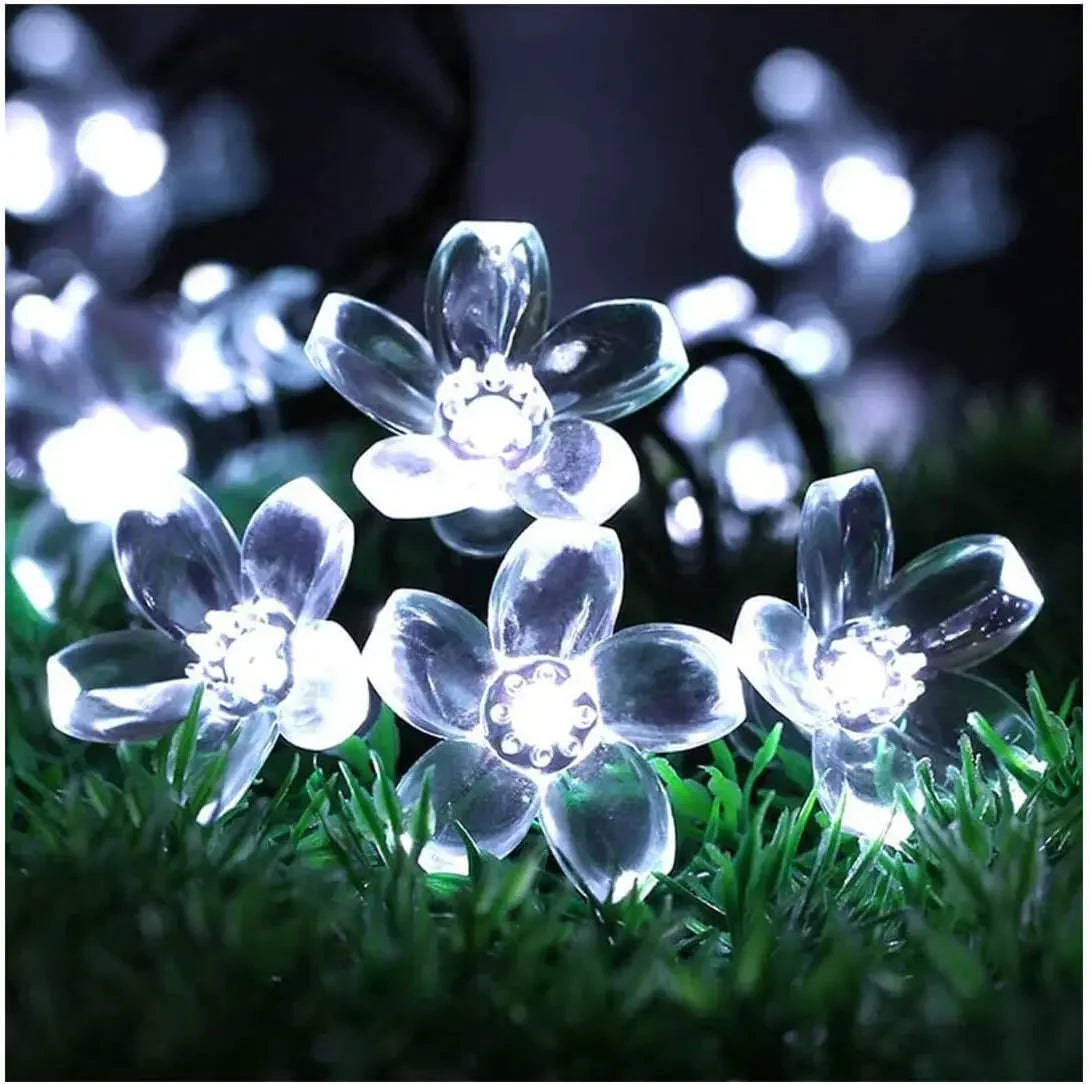 Clear plastic flower-shaped string lights glow brightly on grass, creating a serene and enchanting night scene with soft illumination against a dark background.