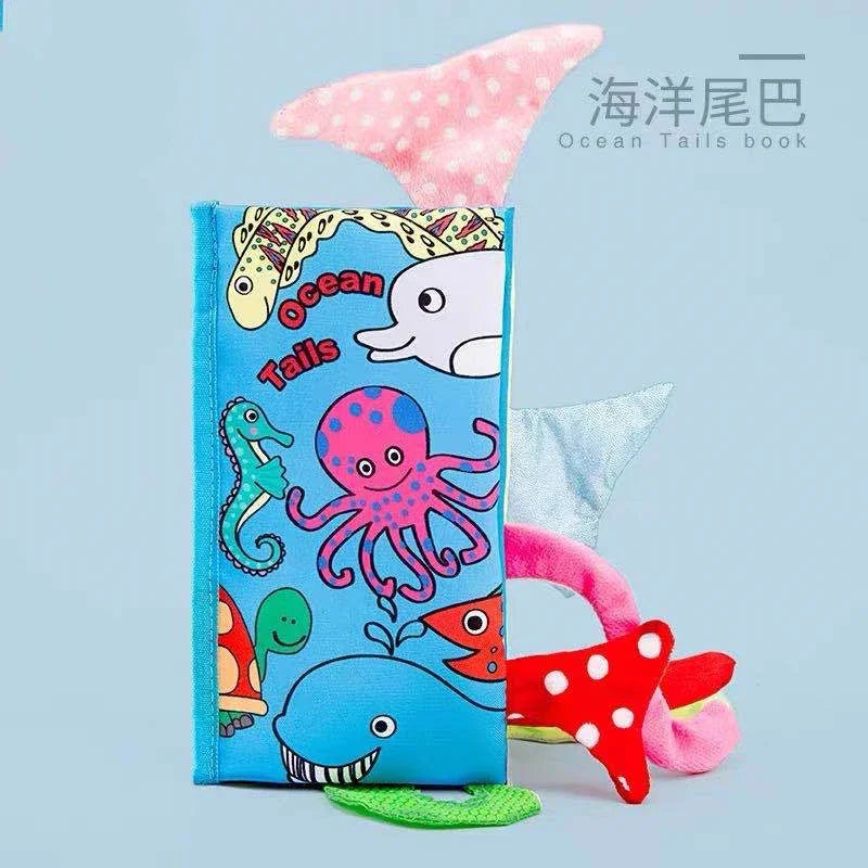 Children's fabric book titled "Ocean Tails" with colorful sea creatures, like an octopus and dolphin, on a blue cover. Various textured tails protrude playfully from the edges.