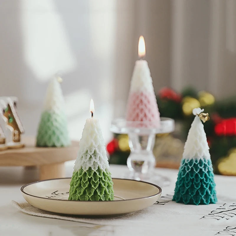 Cone-shaped candles resembling Christmas trees in green, white, pink, and blue hues, with one lit candle on a plate in the foreground, creating a festive atmosphere.