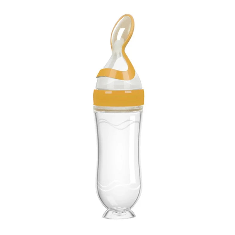 Transparent baby bottle with an orange cap and spoon-shaped tip. The bottle has a curvy design and a small round base.