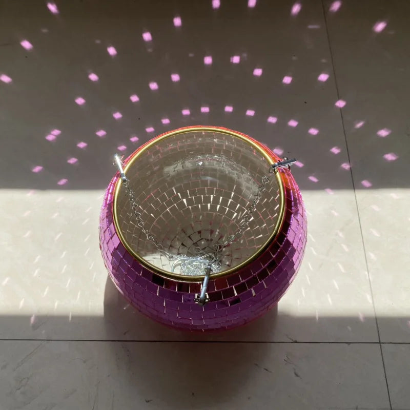 A pink disco ball on the floor reflects sunlight, casting scattered pink light patterns on the surrounding area.