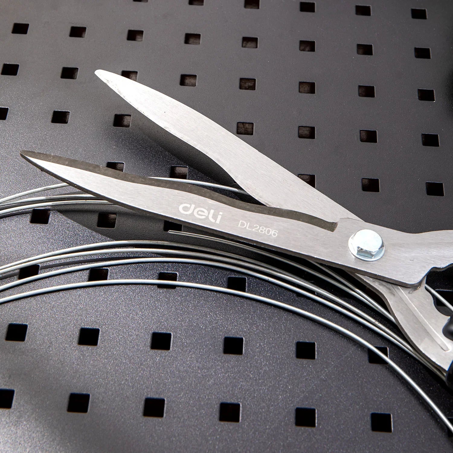 Close-up of a pair of stainless steel deli scissors labeled "DL2806," lying on a perforated black surface. Several metal wires are beneath the scissors' blades.