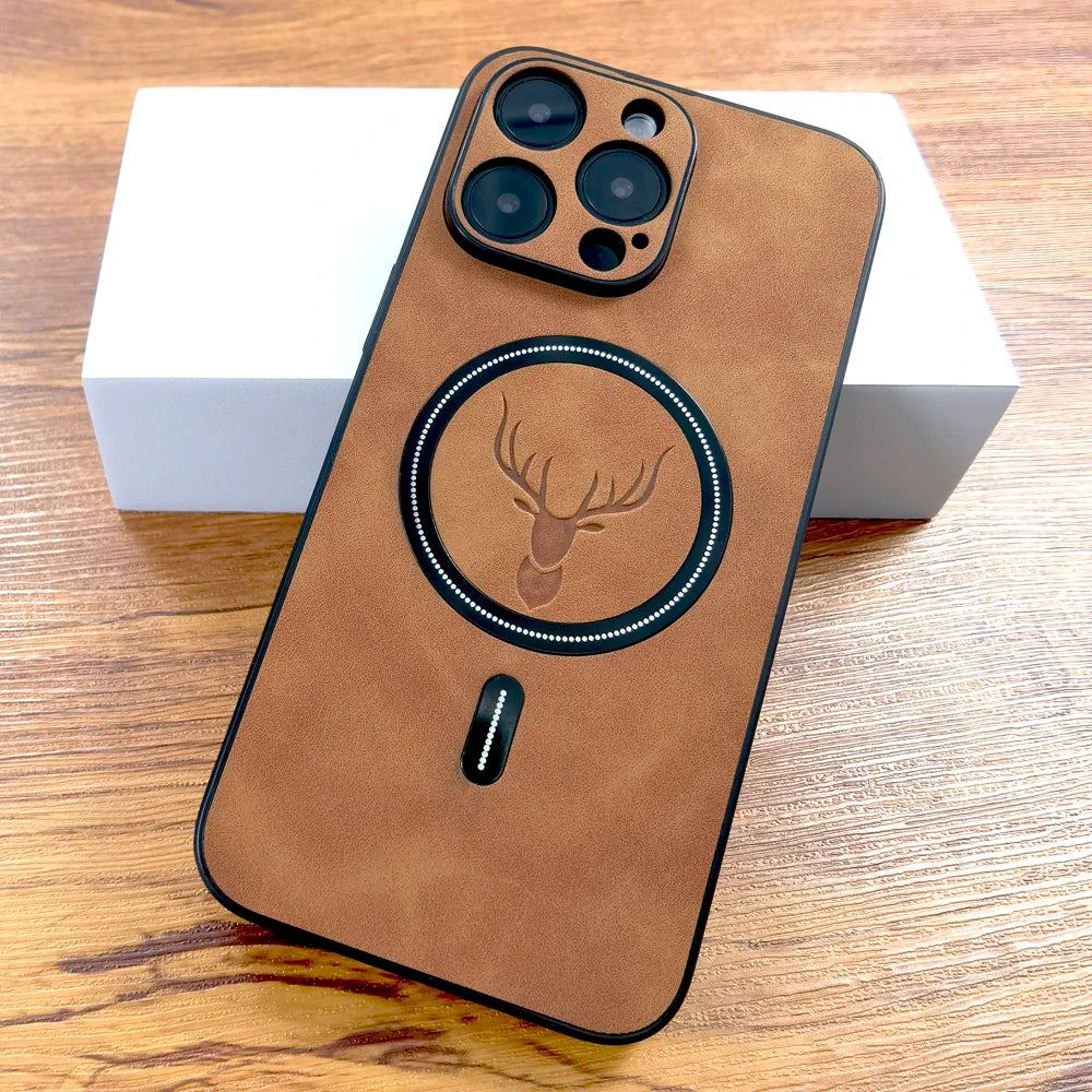 Brown leather phone case with camera cutouts and an engraved deer head design centered around a circular ring. The case rests on a white box on a wooden surface.