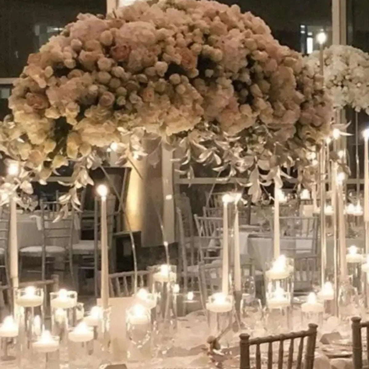 Elegant wedding reception with large floral centerpiece, featuring white and blush flowers. Tall candles and soft lighting create a romantic, sophisticated atmosphere.