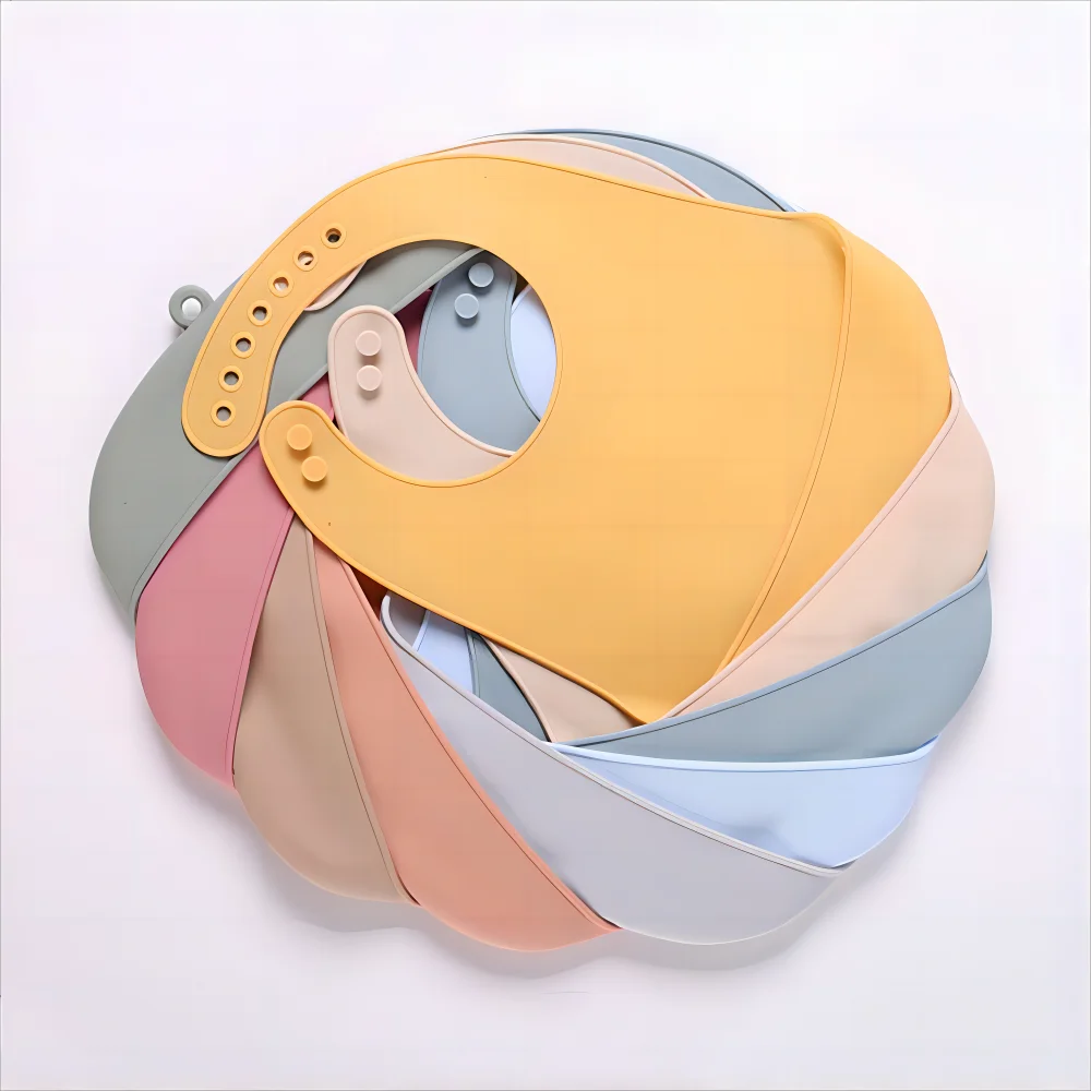 A neatly arranged spiral of multicolored silicone baby bibs in pastel shades of pink, blue, yellow, and beige, showcasing their adjustable straps and soft material.