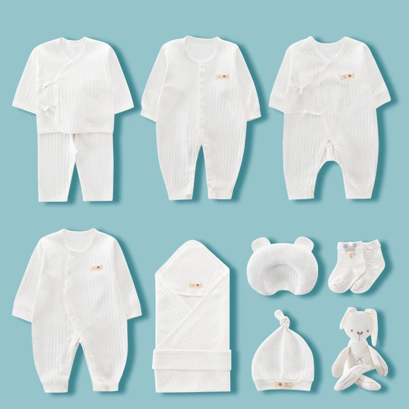 A set of white baby clothing and accessories on a blue background, including onesies, a wrap, socks, a hat, a bear-shaped pillow, and a plush toy.