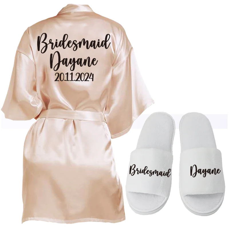 A satin robe with "Bridesmaid, Dayane, 20.11.2024" printed on the back, paired with white slippers labeled "Bridesmaid" and "Dayane."