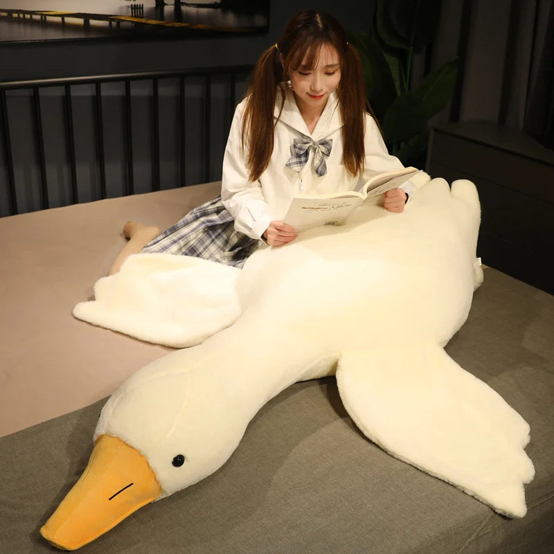 A woman with pigtails reads a book while sitting on a bed, leaning against a large plush duck. The room is warmly lit, adding a cozy ambiance.