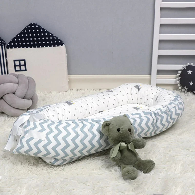 Cozy baby nook with blue chevron pattern blanket, plush teddy bear, star-patterned pillows, and soft carpet in a nursery.
