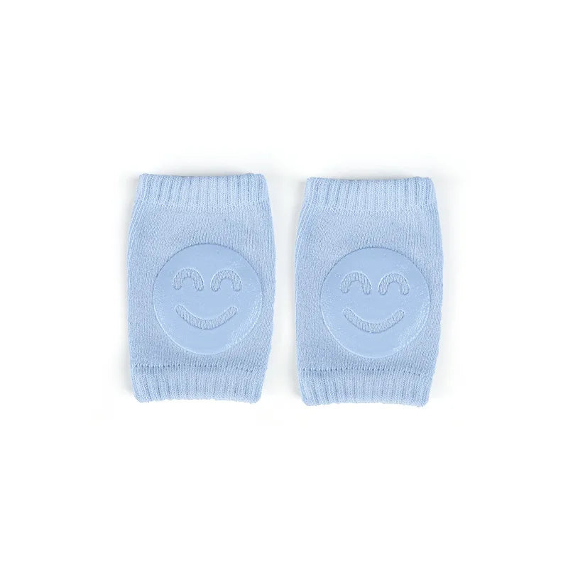 Light blue knee pads with smiling face design on a white background. Made from soft fabric, they provide cushioning and comfort for crawling babies.