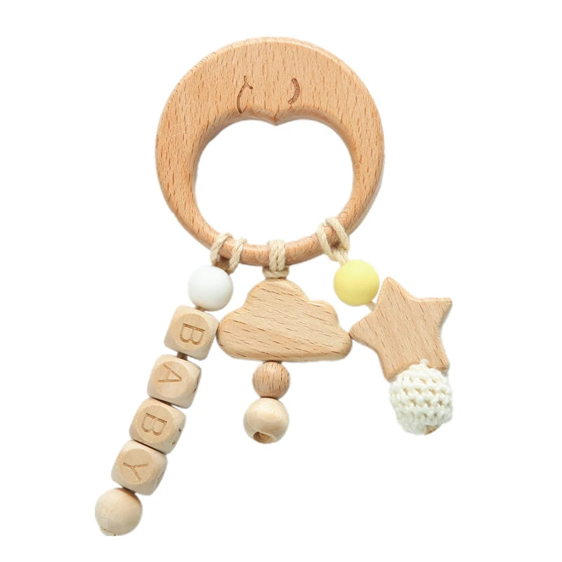 Wooden baby teething toy with a moon-shaped handle, adorned with a cloud, star with crochet detail, and beads spelling "BABY.", featuring mixed materials for sensory play.