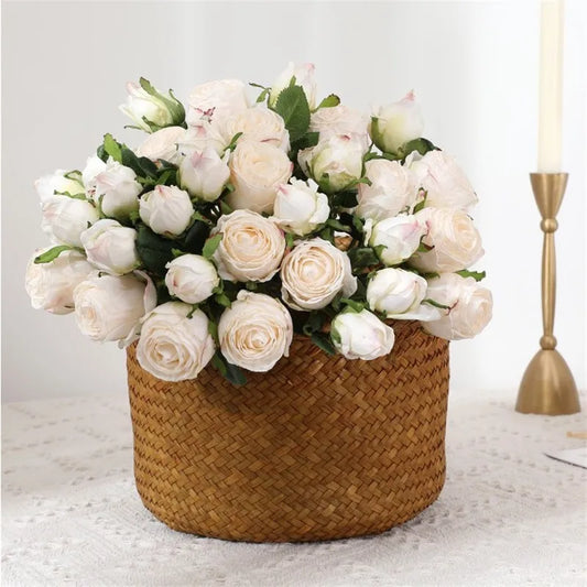 A woven basket filled with creamy white roses with green leaves, set on a lace tablecloth. A gold candlestick is visible on the right, suggesting an elegant setting.