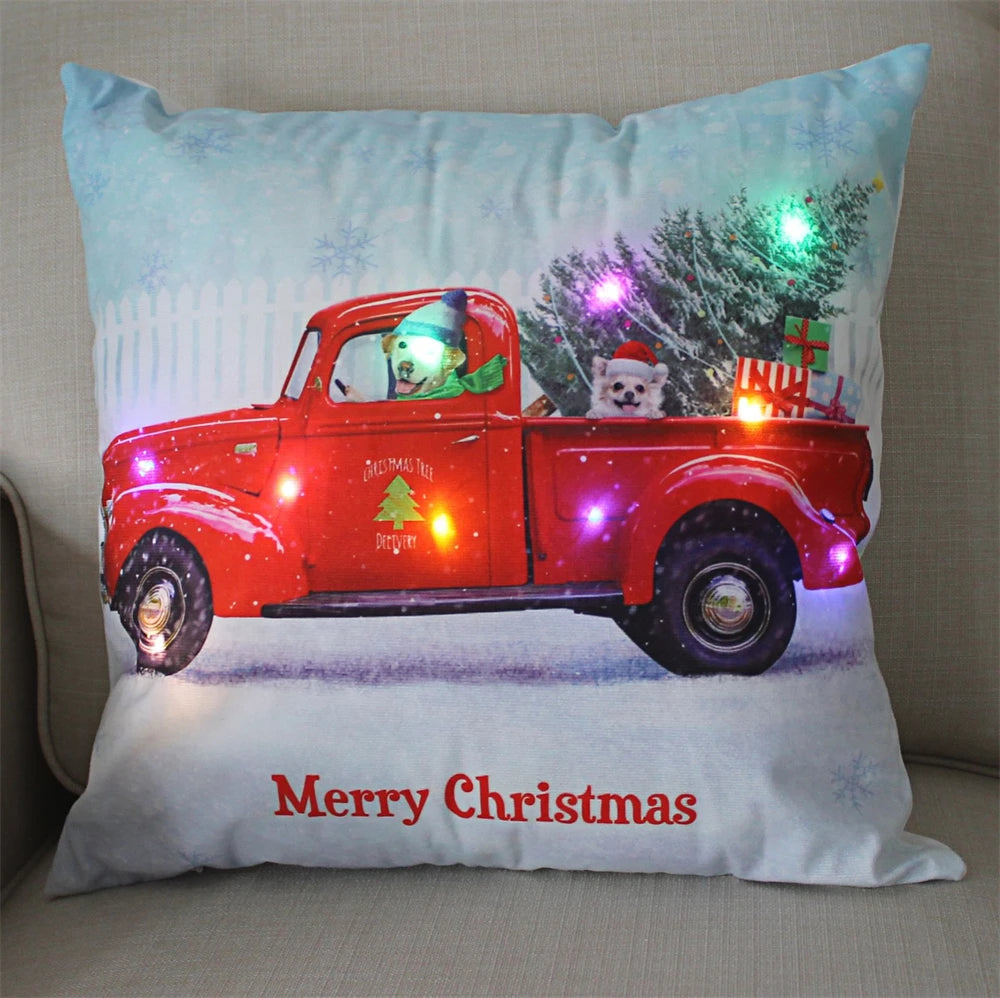 Festive pillow with dogs in a red truck, carrying a Christmas tree and gifts. The scene is decorated with colorful LED lights and a "Merry Christmas" message below.