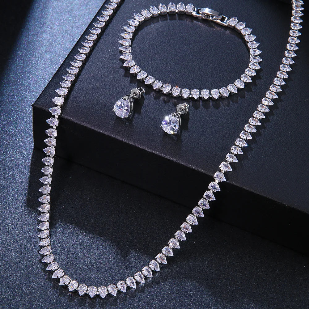 Elegant jewelry set with a sparkling teardrop design, featuring a gold necklace, matching bracelet, and dangling earrings, displayed on a black surface.