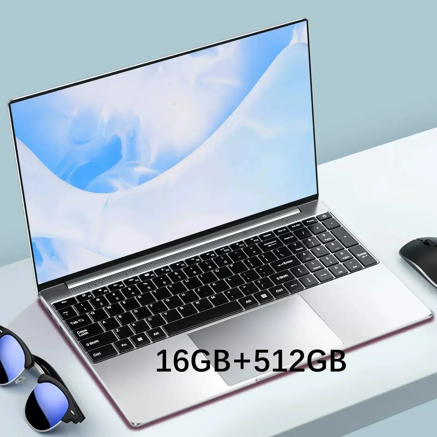 Sleek silver laptop on a light blue desk with a black keyboard, thin bezels displaying an abstract blue wallpaper. Beside it are sunglasses and a mouse. Text reads "16GB+512GB."