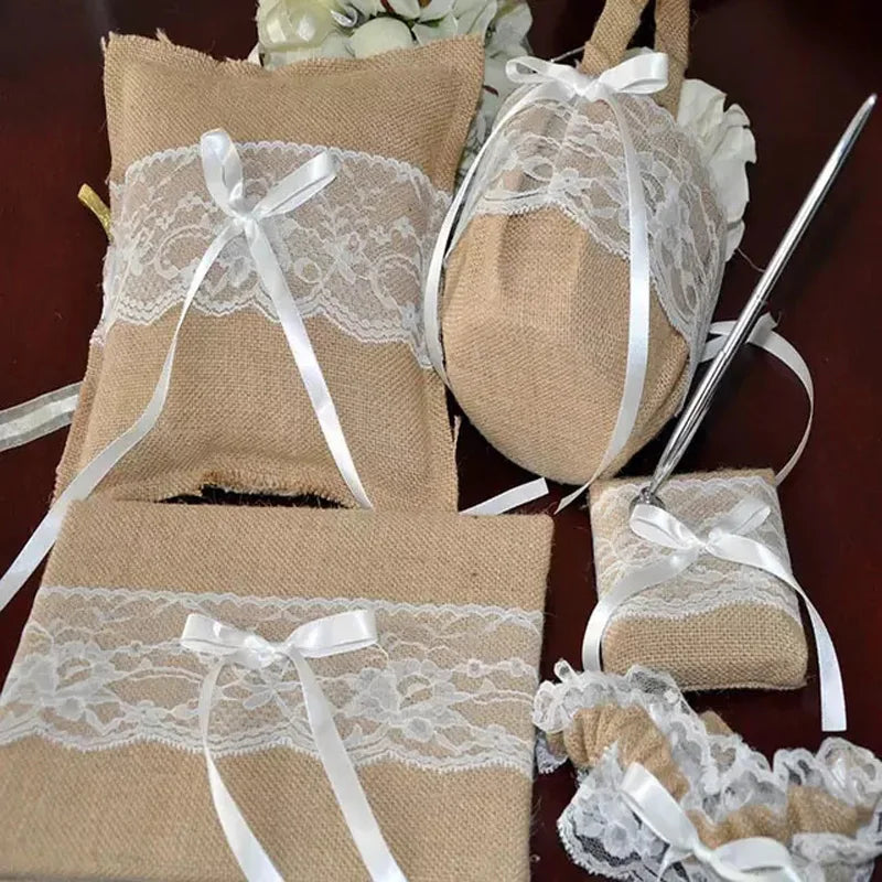 Rustic wedding accessories set with burlap and lace designs, featuring a ring pillow, guestbook, pen holder, and garter, all adorned with white ribbon bows.