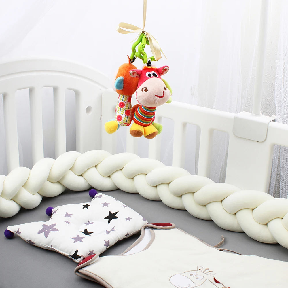 A cozy crib setup with a braided bumper, hanging plush toys, a star-patterned pillow, and a small blanket, conveying a playful and soothing nursery environment.