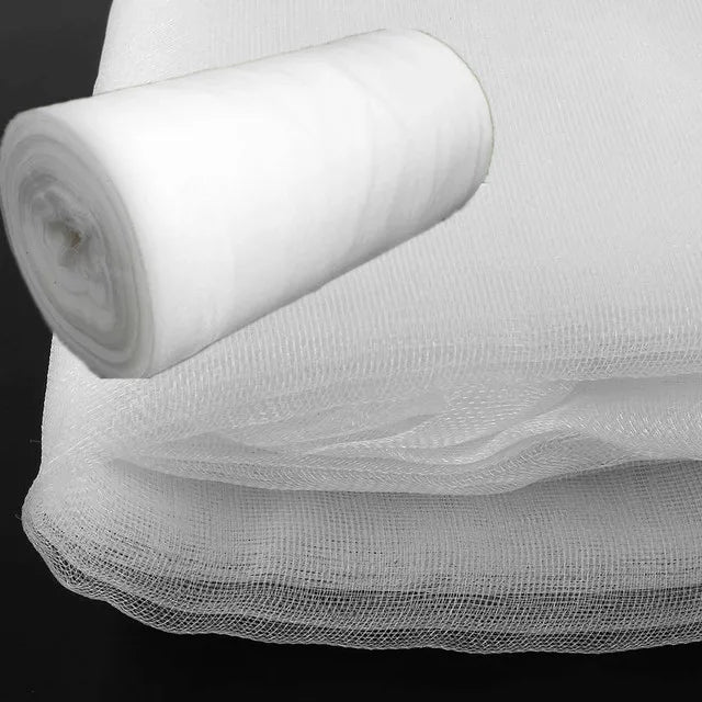 Roll and stack of white tulle fabric on a dark background, showcasing its translucency and soft texture.