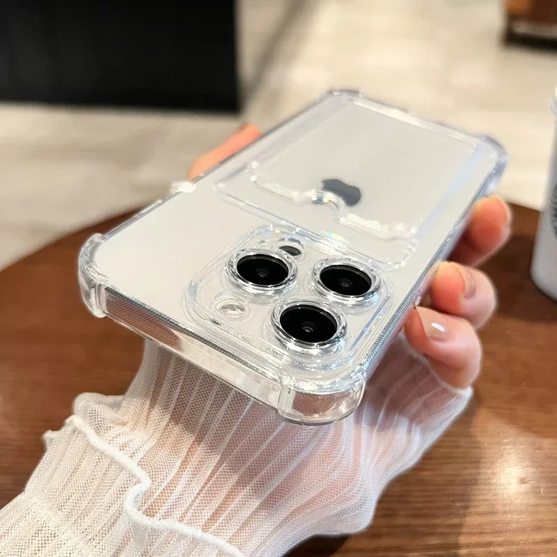 A hand holding a smartphone with a clear case, featuring three prominent camera lenses. The phone is resting on a wooden table with a blurred background.