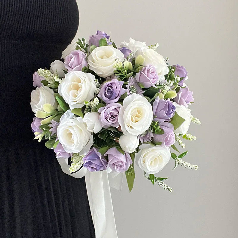 A person holds a bouquet of white and lavender roses with greenery, tied with a white ribbon, against a plain light background, contrasting with their dark clothing.
