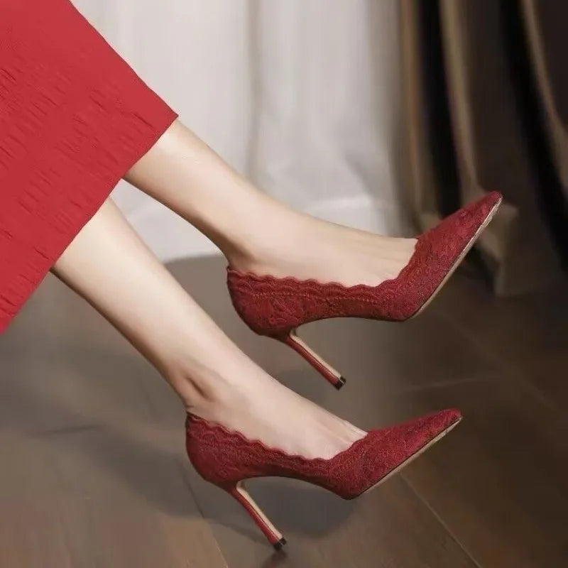 Elegant red lace high heels with pointed toes and stiletto heels worn with a matching red dress, stylishly posed on a wooden floor, creating a chic and sophisticated look.