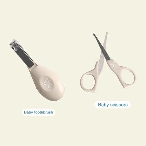 A beige baby toothbrush and a pair of baby scissors, each labeled, on a light background. The toothbrush has a teardrop shape handle, and the scissors have rounded tips.