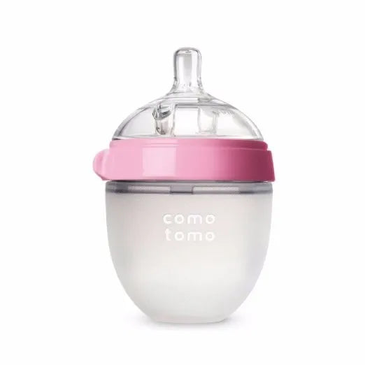 A silicone baby bottle with a wide-neck design and pink collar, featuring a clear nipple and the text “como tomo” on the frosted white body.