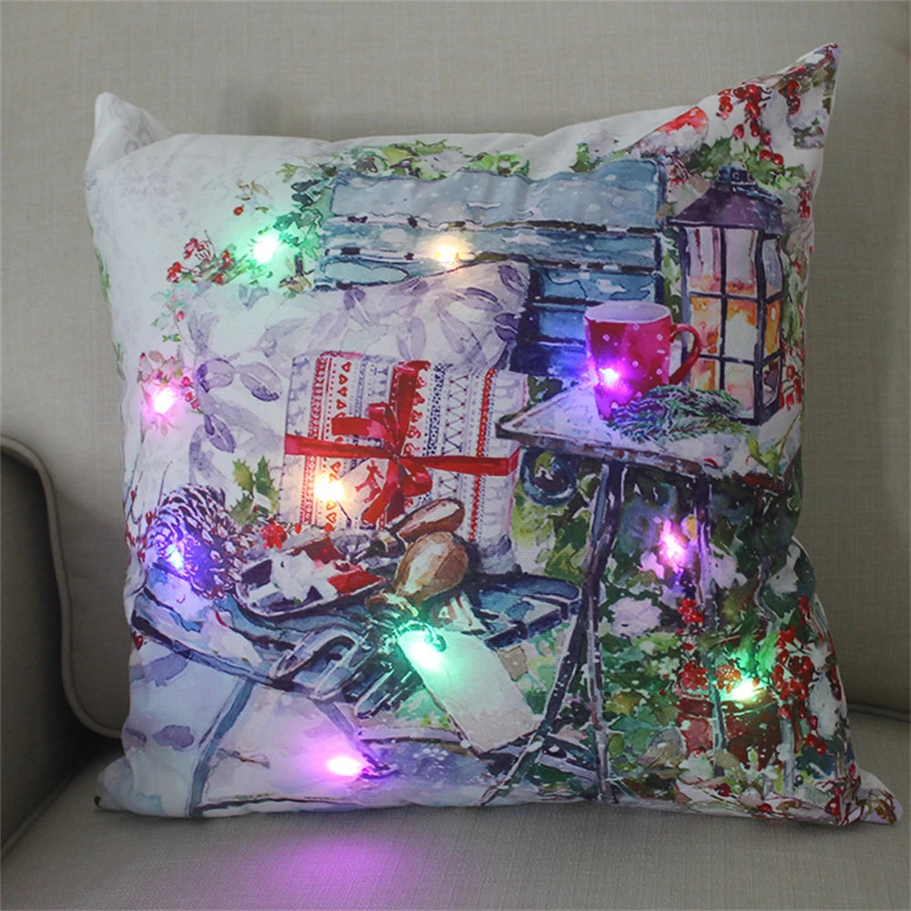 Festive pillow with a snowy outdoor scene, featuring a red mug, gifts, and a lantern. LED lights in various colors highlight the design on a beige couch.