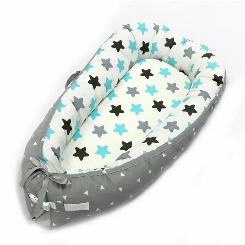 Gray and white baby nest with teal and black star patterns, featuring a bow at the bottom. The cushioned sides form a cozy, oval shape for a comfortable sleeping area.