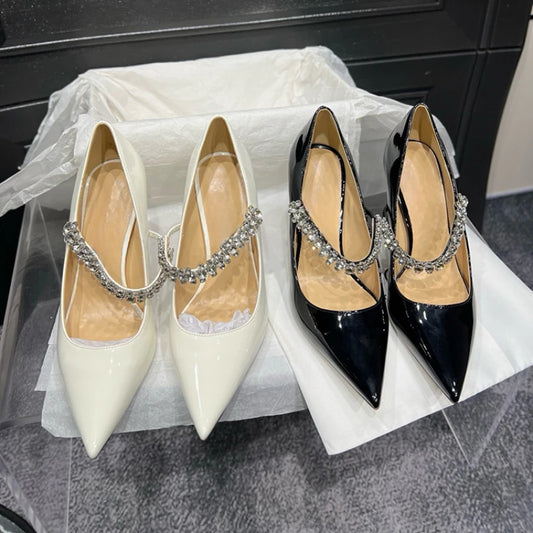 Two pairs of pointed-toe high heels with rhinestone ankle straps, one in glossy white and the other in glossy black, displayed on white tissue paper in a box.