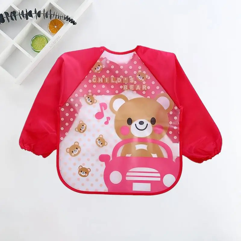 Child's red smock with a cute bear driving a car, musical note, and polka dots. Shelves with black branch and citrus slices are visible in the background.