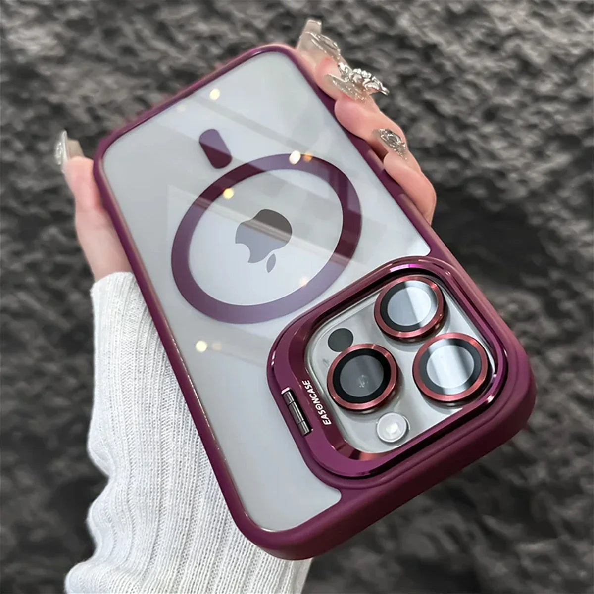 A hand holds a smartphone with a purple-framed, translucent case that reveals an apple logo. The case features three prominent camera lenses with matching purple rings.