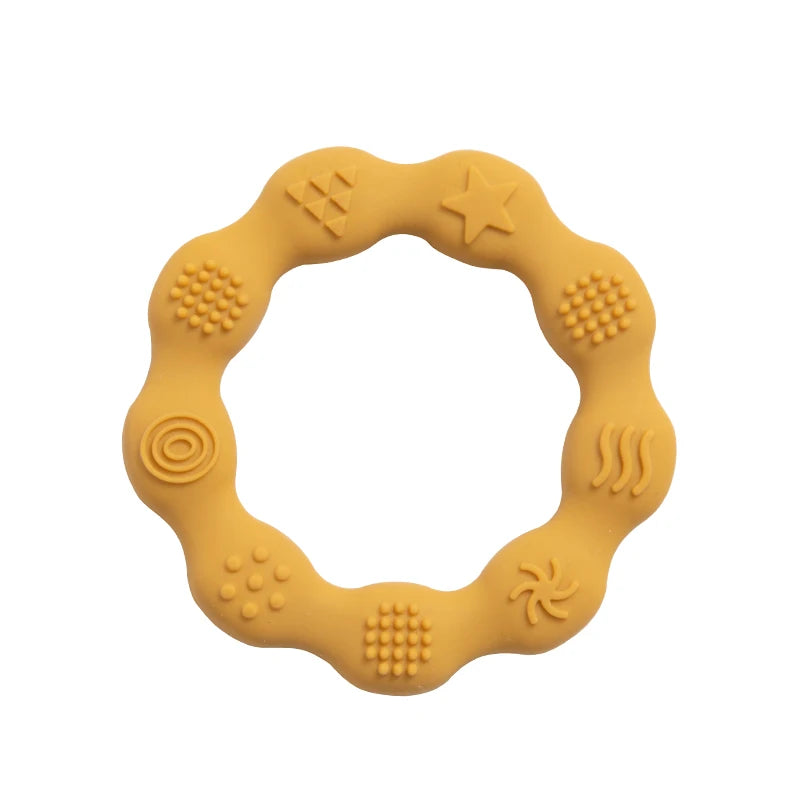 A round mustard-colored teething ring with a wavy edge features various embossed patterns, including a star, circles, and textured dots, designed for tactile stimulation.