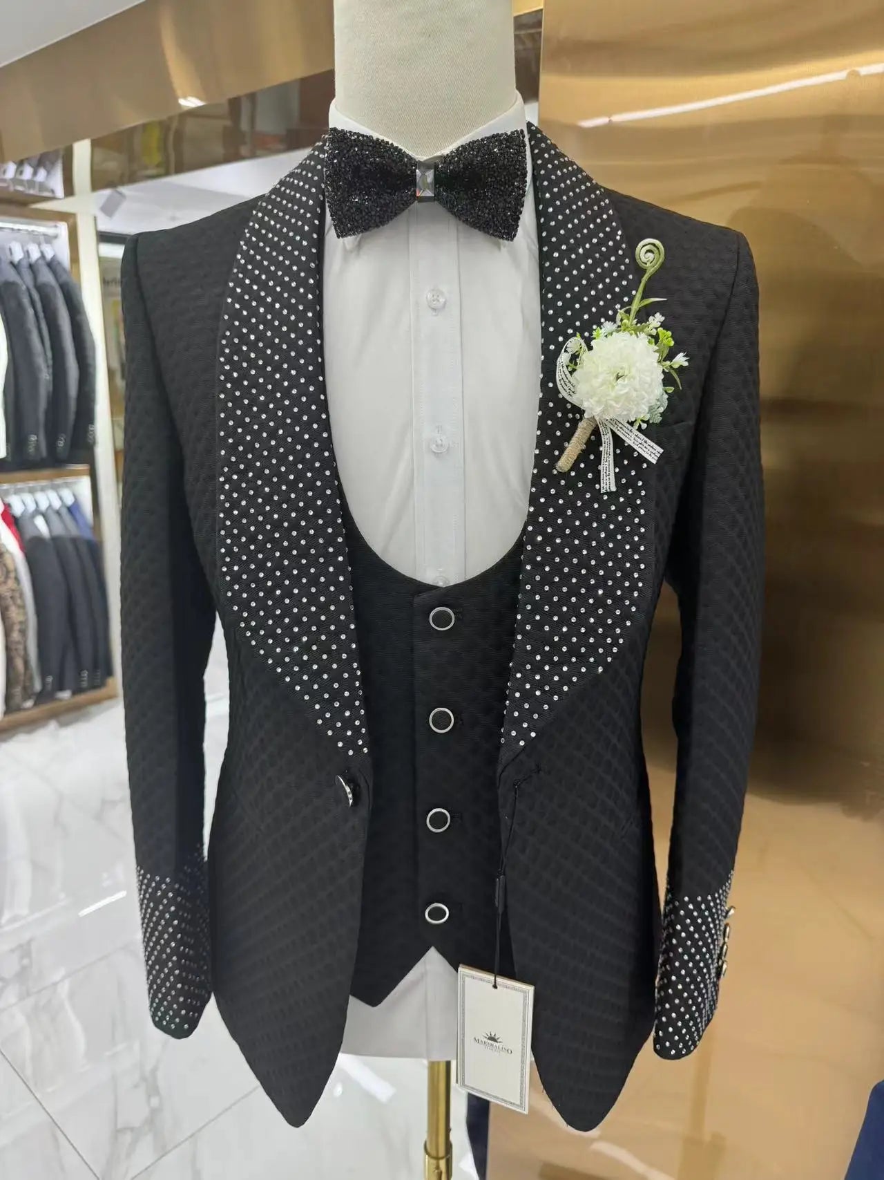 Elegant black tuxedo with a textured pattern, featuring polka-dot lapels, cuffs, and pocket square. It includes a black sequined bow tie and a white floral boutonniere.