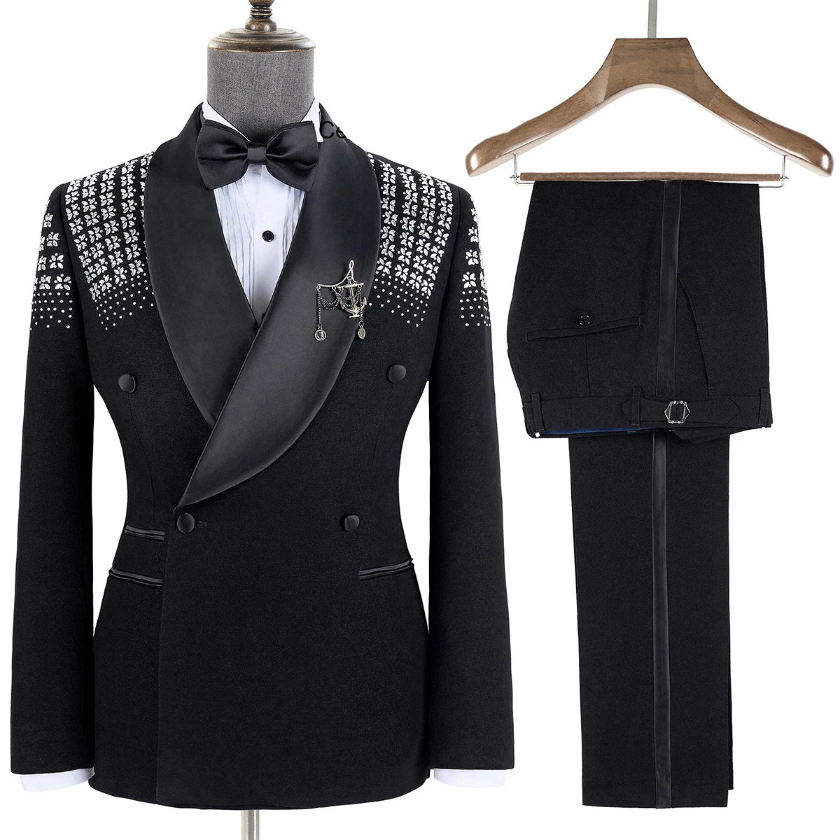 Elegant black tuxedo with embroidered shoulders, satin shawl lapel, and double-breasted design. Paired with matching black pants on a wooden hanger and accessorized with a bow tie.