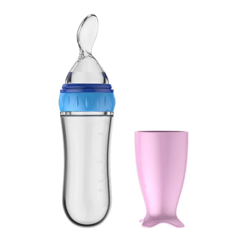Clear baby feeding bottle with a blue lid and attached spoon, alongside a pink cover.