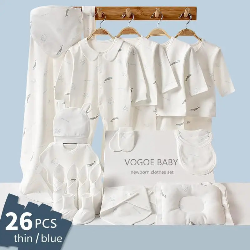 Baby clothes set for newborns displayed on wooden hangers, including tops, mittens, hats, and more. White with subtle prints. Box labeled "Vogoe Baby," totaling 26 pieces.