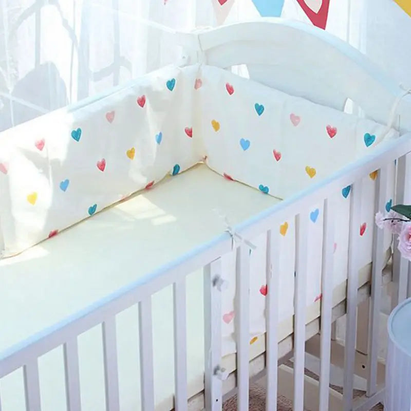 White baby crib with colorful heart-patterned bedding. The crib has side bumpers for safety, and soft natural light illuminates the space, creating a serene atmosphere.