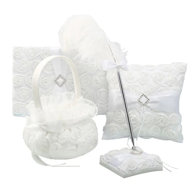 Elegant white wedding set with a flower basket, guest book, pen with stand, and ring pillow, all adorned with white lace roses and decorative silver accents.