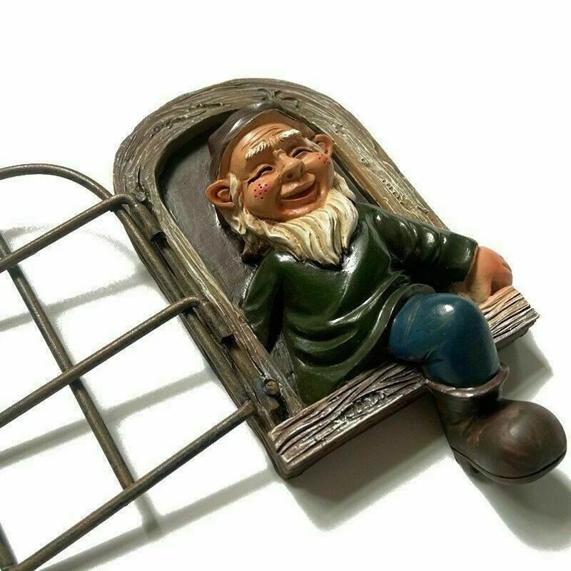 A cheerful garden gnome figurine with a white beard and red cheeks, wearing a green coat and blue pants. It sits by a small arched window with a metal fence beside it.