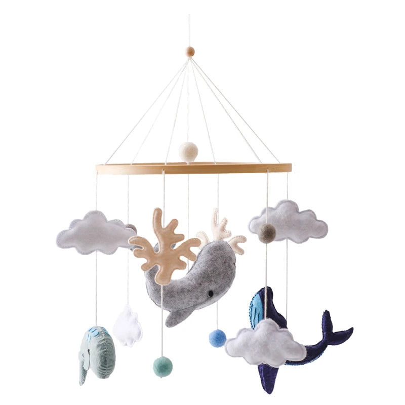 Wooden mobile with hanging felt animals: whale, elephant, and narwhal, surrounded by clouds and small pompoms. Ideal for a baby's nursery with a soothing, whimsical design.