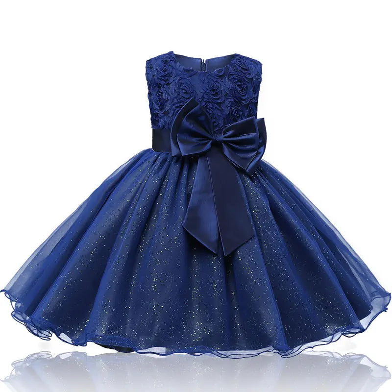 Elegant blue dress with a floral lace bodice, satin waistband, and large bow. The full skirt is adorned with shimmering accents, creating a stylish, festive look.