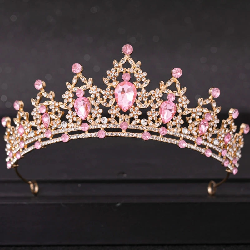 A gold tiara adorned with large pear-shaped and round pink gems, intricately arranged with smaller clear stones, set against a dark background.