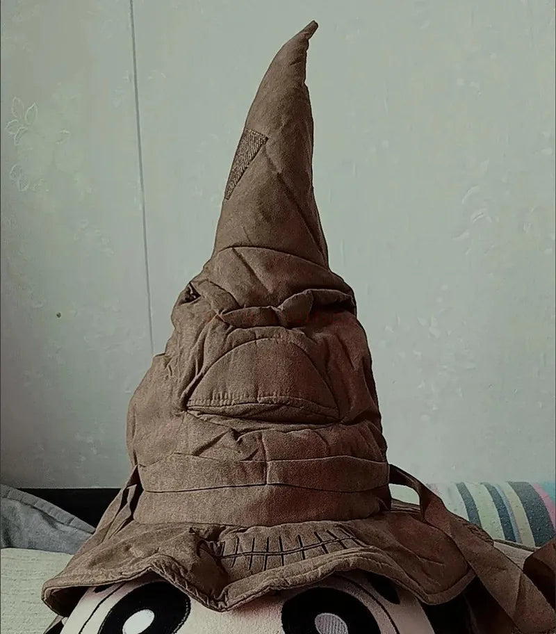 A brown, wizard-like hat with a pointed tip and a face-like expression rests atop a round, wide-eyed object, set against a simple, pale background.